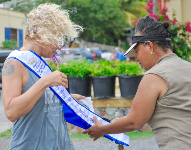 Parade organizer Judi Shimel drapes the parade marshal sash on a wind-buffeted Nancy Stromp before the Coral Bay Labor Day parade.