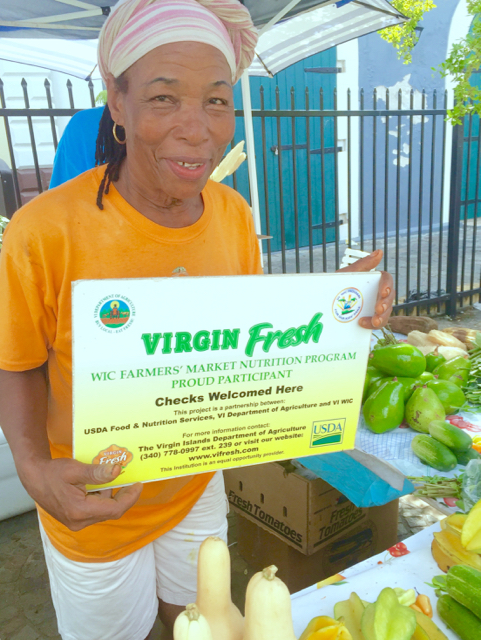Drina Anthony displays signs that show where the new food assistance benefit can be used at the Market Square farmers market on St. Thomas.