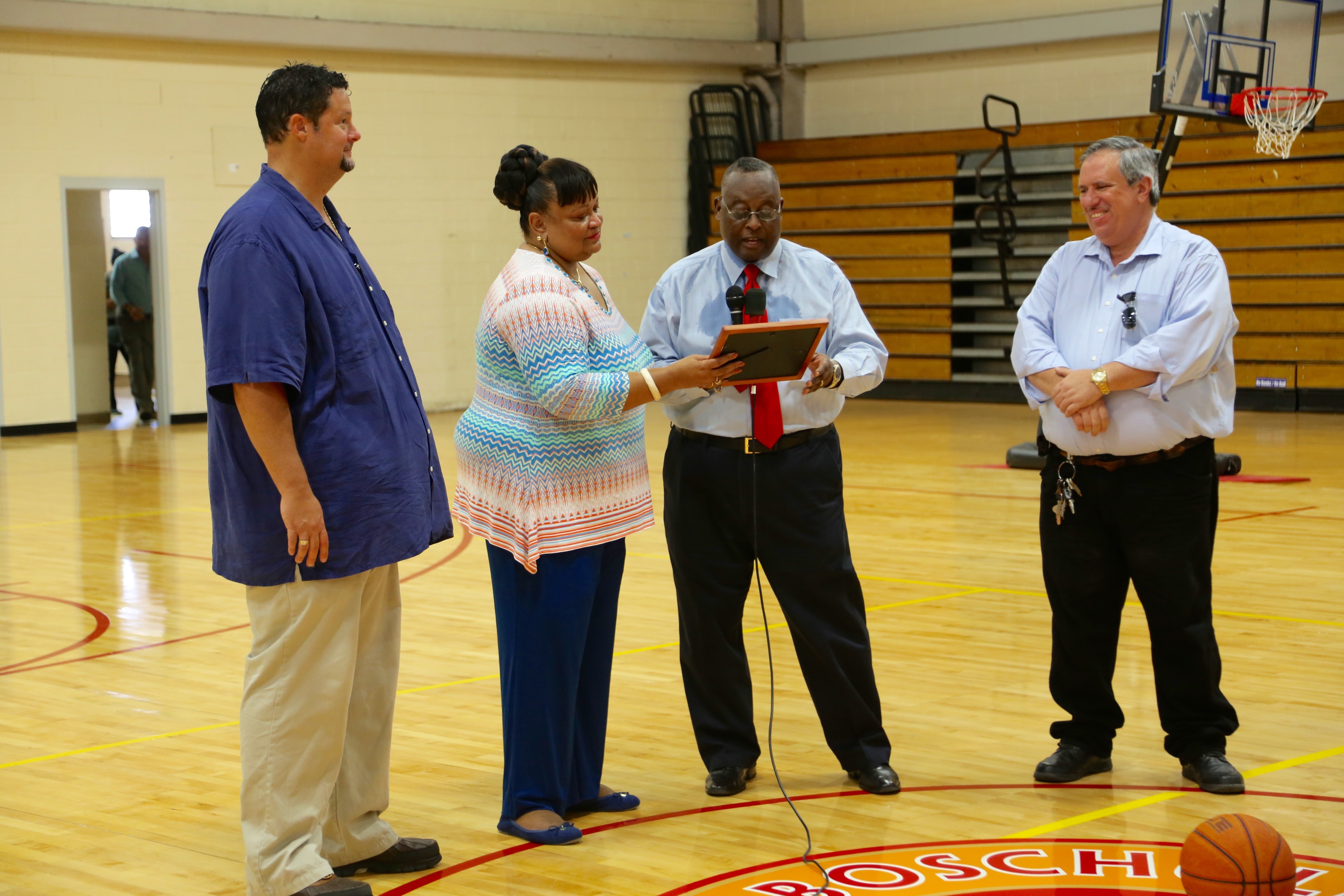 BCB Middle School Principal Carver Farrow presents Education Commissioner Sharon Ann McCollum with a certificate of appreciation at the unveiling of the school&rsquo;s new hardwood basketball floors on Aug. 31. Peter Seipel, left, territorial director of athletics. and James Bernier, right, territorial director of capital projects and facilities, look on.