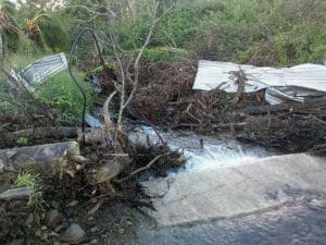 Water flows through a gut in LaGrange after Hurricane Maria last fall, leaving galvanized roofing and other storm victims behind. (Photo by Julie Wright)