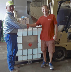 David Wallis, left, of the Limetree Bay Refinery Logistics Team, takes receipt of the first order of Breadfruit Alcohol Surface Sanitizer from Master Distiller Art Wollenweber of Mutiny Island Vodka. (Submitted photo)