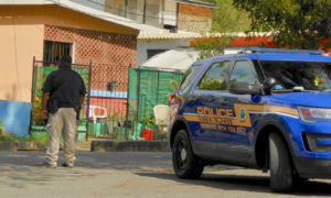 A police officer looks into a yard at the entrance to Hospital Ground. (Source photo by S. Pennington)