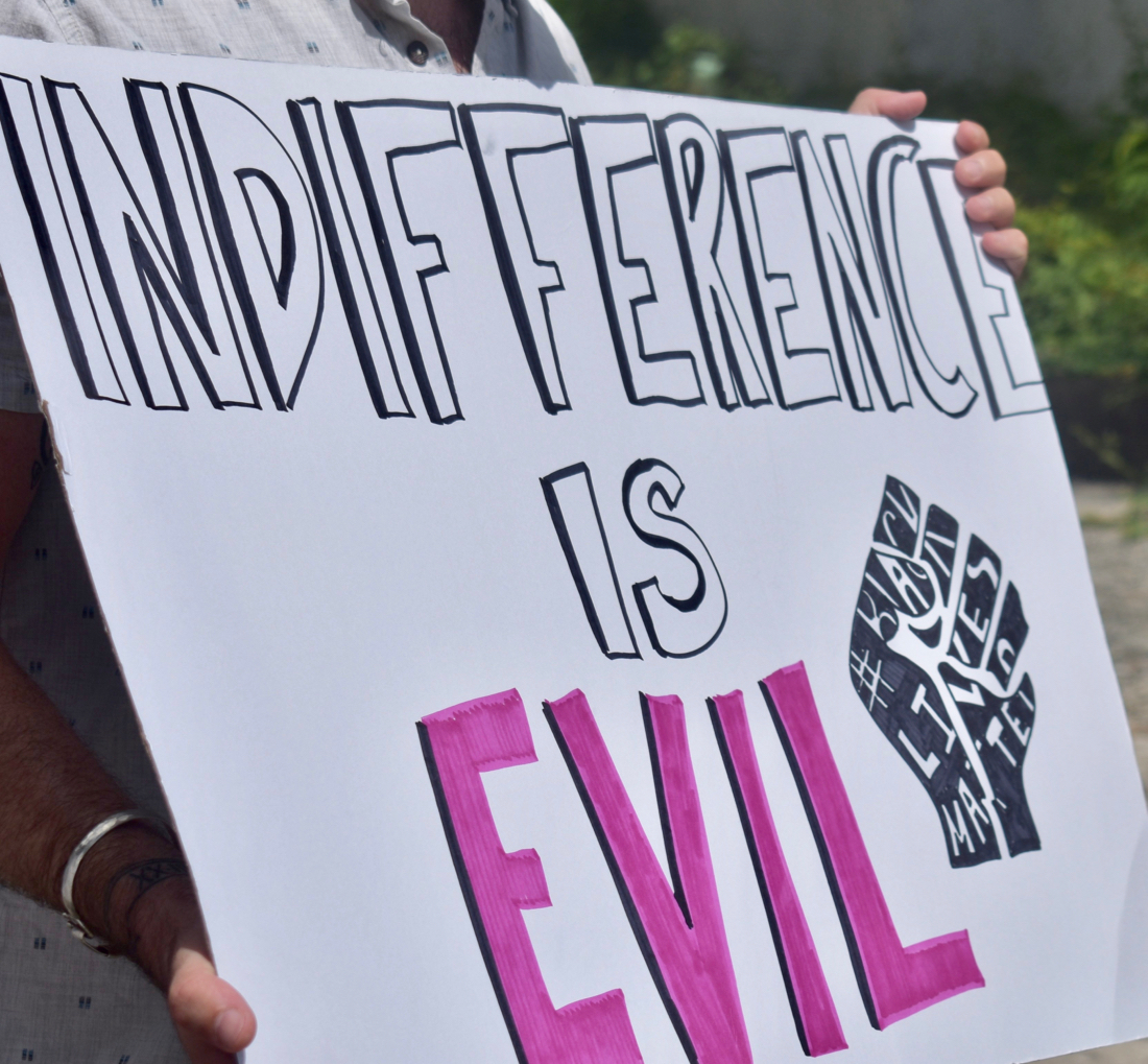 A protester holds up a sign declaring "Indifference is Evil." (Source photo by Kyle Murphy)
