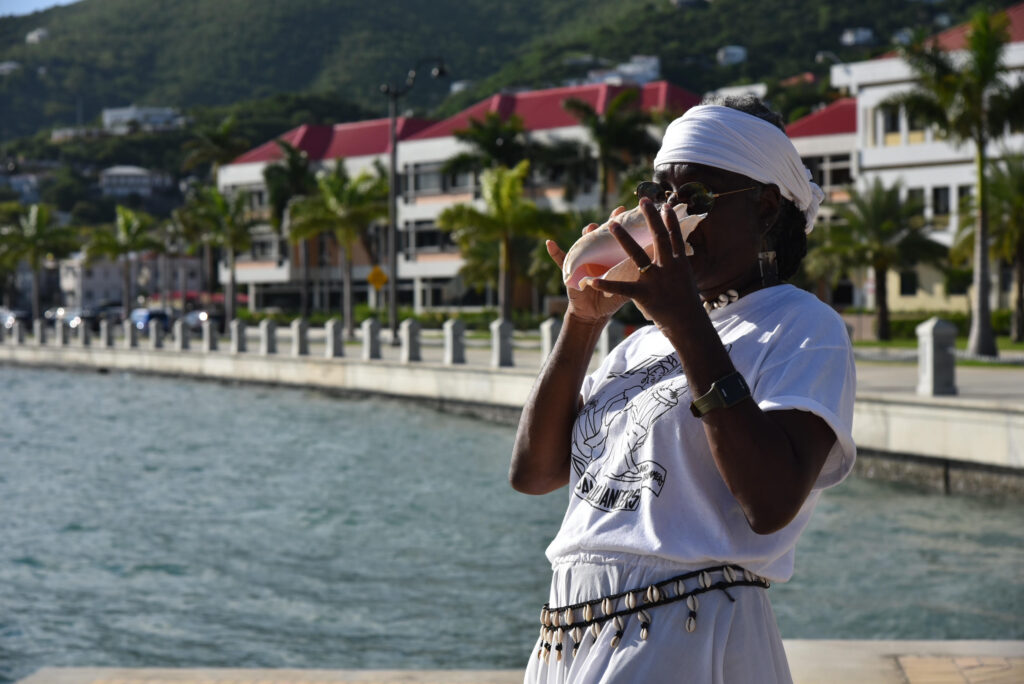 Leniese Mercer of the Ulla Muller Bamboula Dancers and Drummers blows a conch shell at the St. Thomas waterfront. (Conch Shell Media, LLC Photo)
