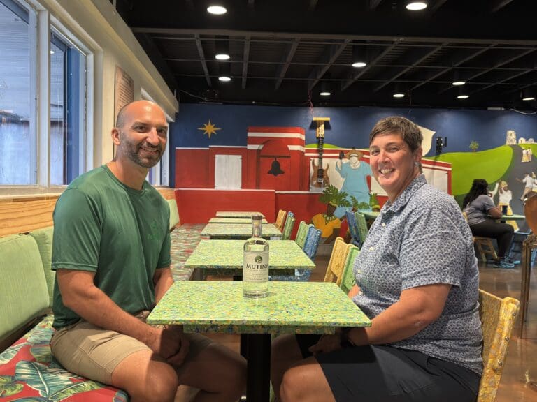 Steve Chmura and Shannon Manns in the Mutiny Vodka dining room seated on chairs with table tops created from recycled plastic by RePlastic Recycle. (Source photo by Susan Ellis)